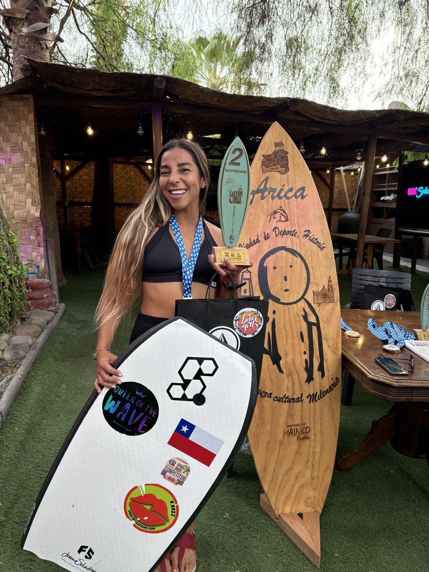 A bodyboarder smiles with her board and trophy board in Arica