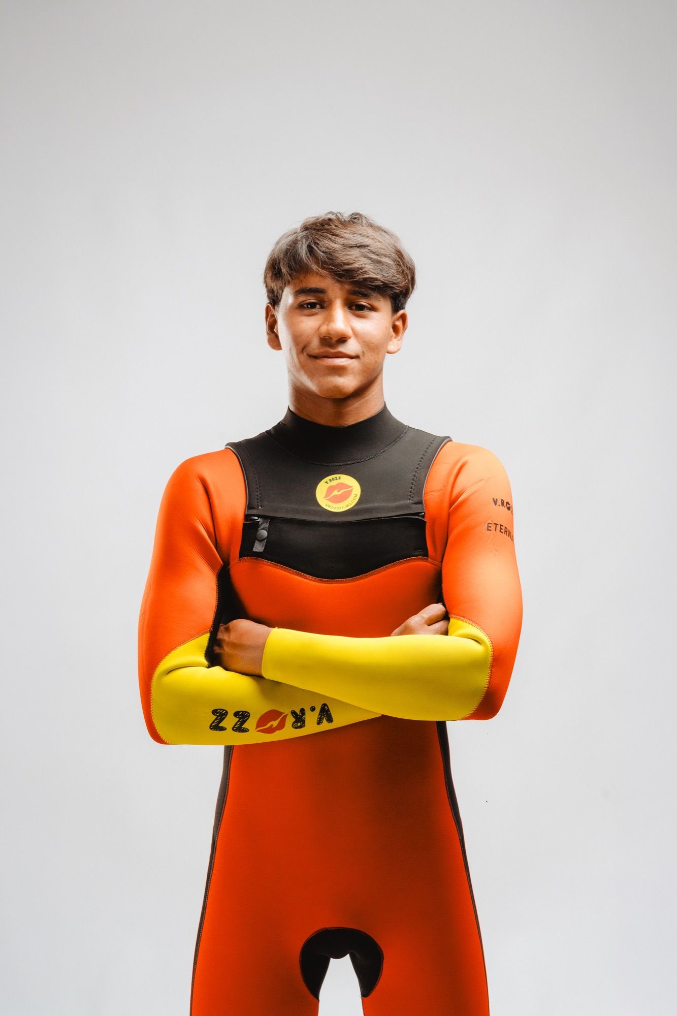 A young surfer in an orange wetsuit, arms crossed